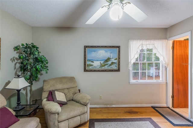 sitting room with light wood-type flooring, ceiling fan, and a textured ceiling