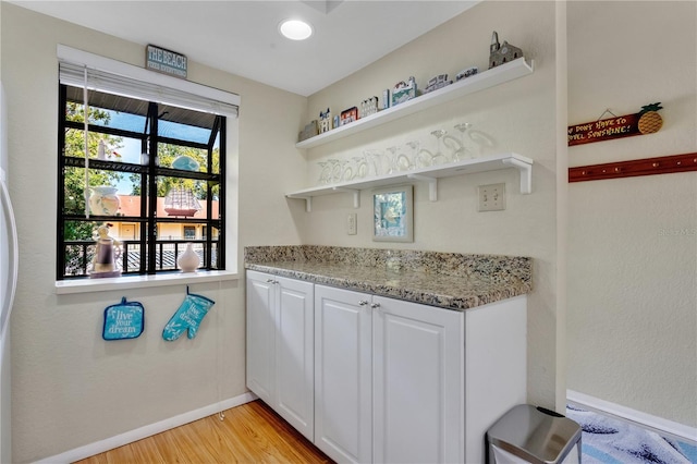 bar featuring light stone counters, white cabinets, and light hardwood / wood-style floors