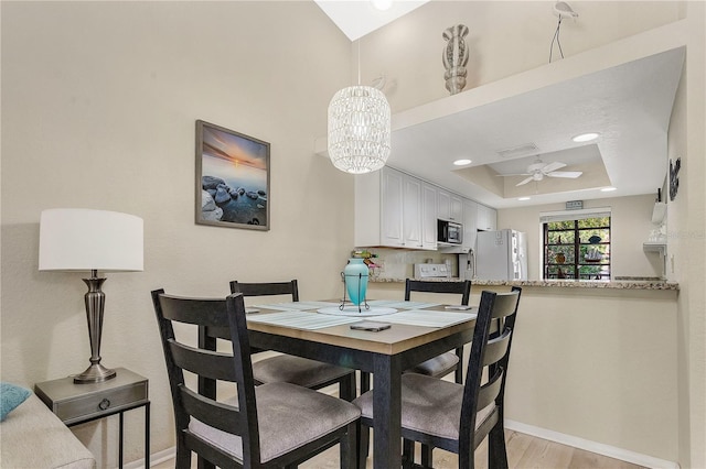 dining room with ceiling fan with notable chandelier, light wood-type flooring, and a tray ceiling