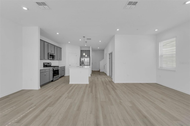 kitchen featuring a center island, light wood-type flooring, appliances with stainless steel finishes, gray cabinets, and pendant lighting