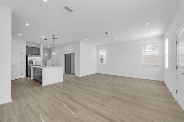 kitchen with gray cabinets, an island with sink, sink, stainless steel fridge, and hanging light fixtures