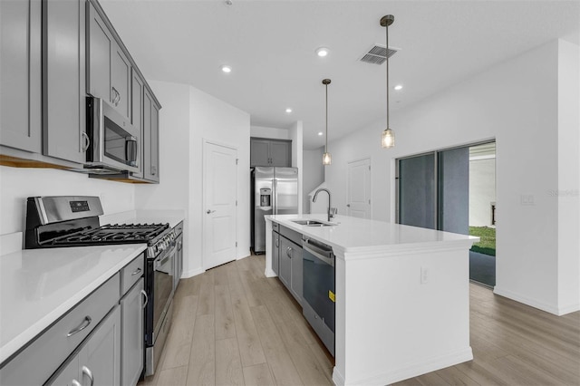 kitchen with appliances with stainless steel finishes, decorative light fixtures, sink, a kitchen island with sink, and light hardwood / wood-style floors