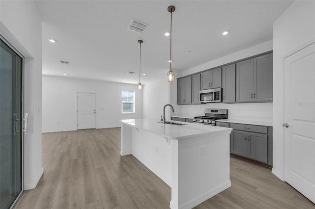 kitchen with sink, gray cabinetry, hanging light fixtures, appliances with stainless steel finishes, and an island with sink