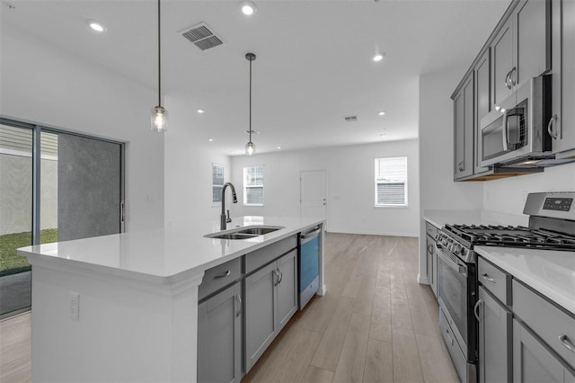 kitchen featuring sink, gray cabinetry, hanging light fixtures, appliances with stainless steel finishes, and an island with sink