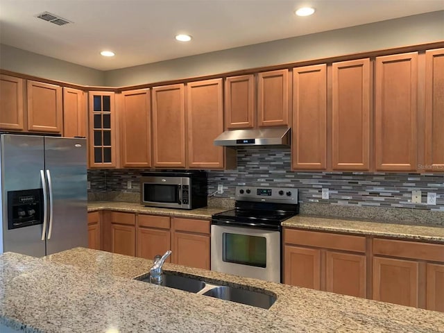 kitchen with light stone countertops, stainless steel appliances, tasteful backsplash, and sink