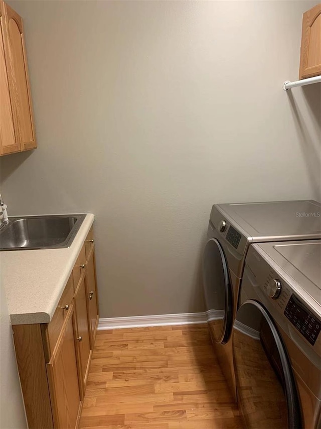 laundry area featuring cabinets, washer and dryer, light hardwood / wood-style floors, and sink