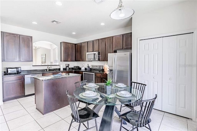 kitchen with appliances with stainless steel finishes, a center island, light tile patterned floors, dark brown cabinetry, and sink