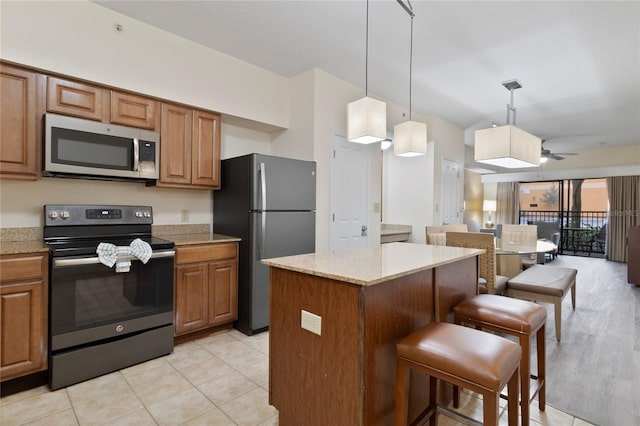 kitchen with a kitchen breakfast bar, appliances with stainless steel finishes, a center island, light stone countertops, and ceiling fan