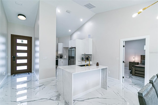 kitchen featuring stainless steel refrigerator with ice dispenser, sink, high vaulted ceiling, white cabinets, and light stone counters