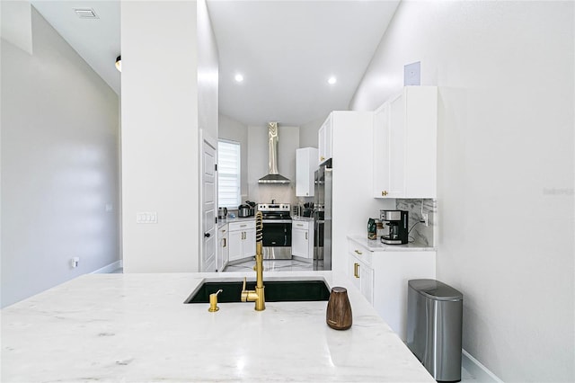 kitchen featuring appliances with stainless steel finishes, white cabinetry, wall chimney range hood, decorative backsplash, and sink