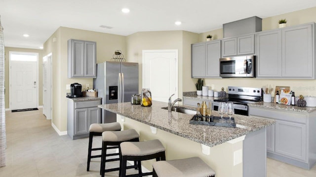 kitchen featuring a breakfast bar area, gray cabinetry, stainless steel appliances, an island with sink, and sink