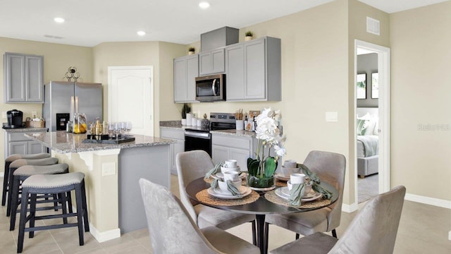 kitchen featuring gray cabinets, stainless steel appliances, a center island, light stone countertops, and light tile patterned floors