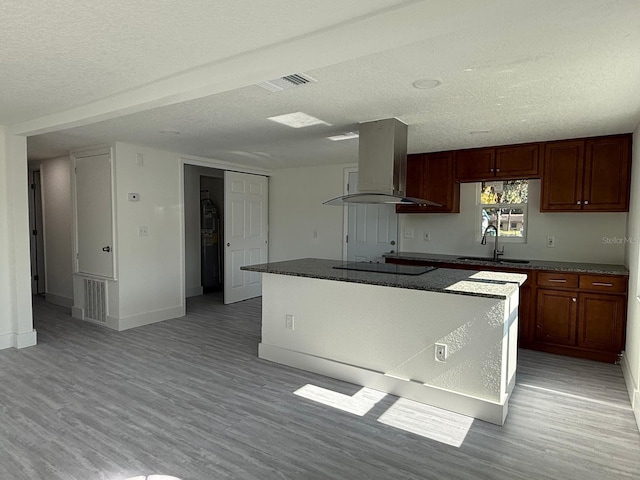 kitchen featuring a textured ceiling, island range hood, a center island, black electric stovetop, and sink