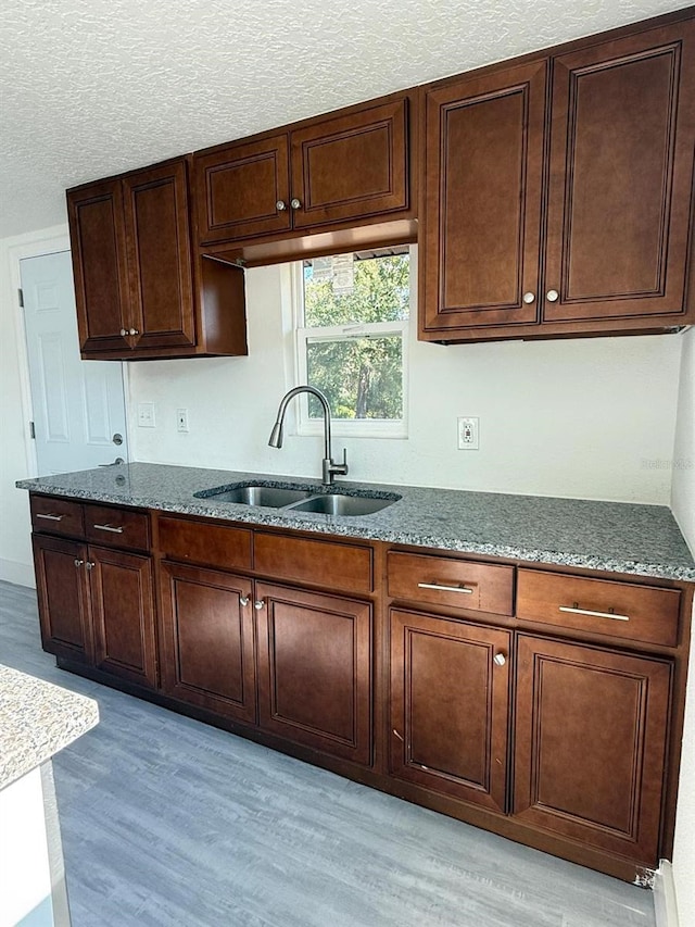 kitchen featuring sink, light wood-type flooring, dark stone counters, and a textured ceiling