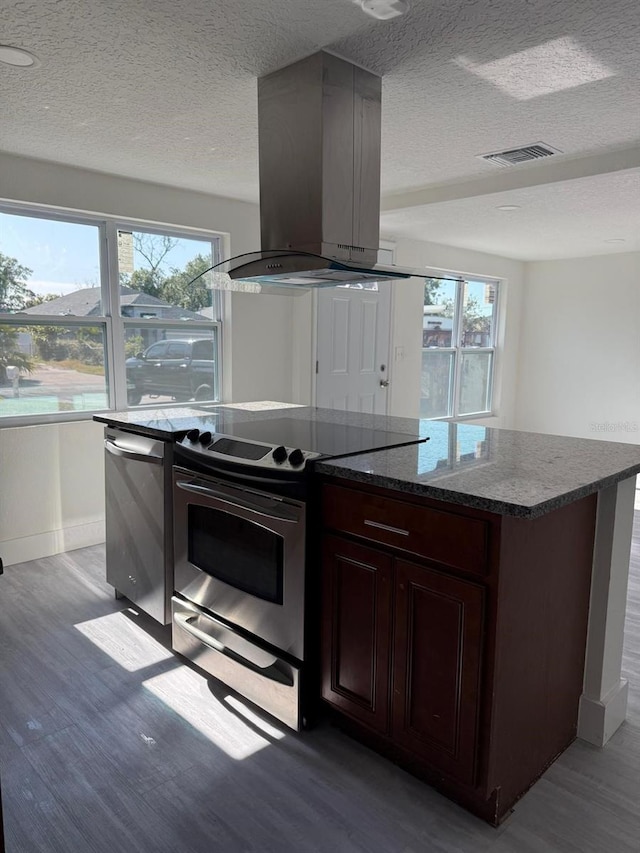 kitchen featuring appliances with stainless steel finishes, island exhaust hood, a healthy amount of sunlight, and light hardwood / wood-style flooring