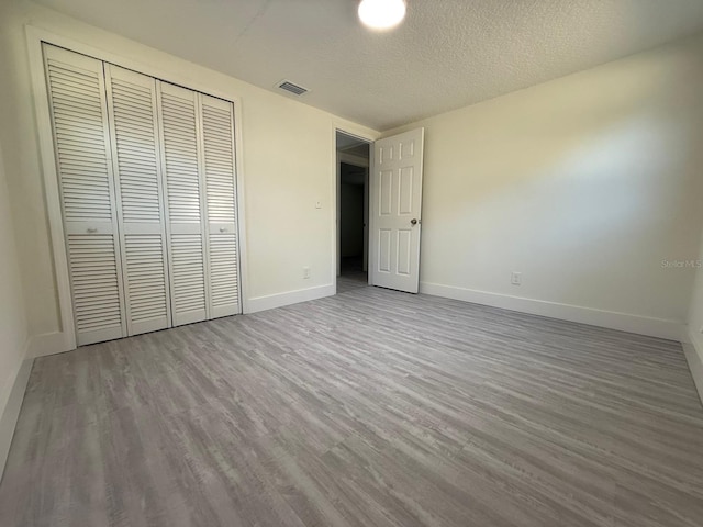 unfurnished bedroom with a textured ceiling, a closet, and light hardwood / wood-style floors