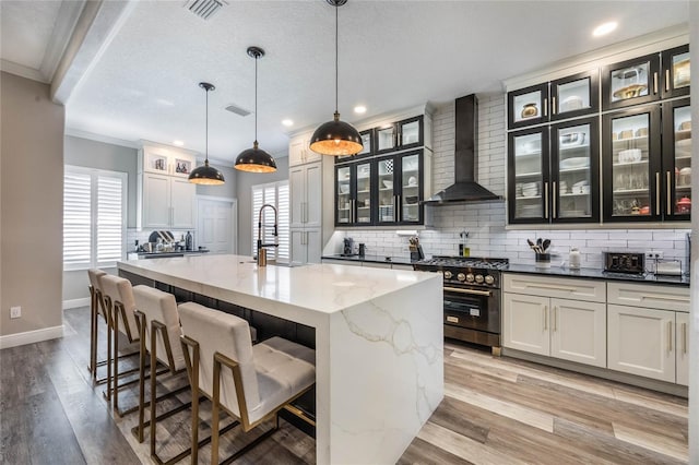 kitchen featuring a large island with sink, backsplash, high end black range, and wall chimney range hood