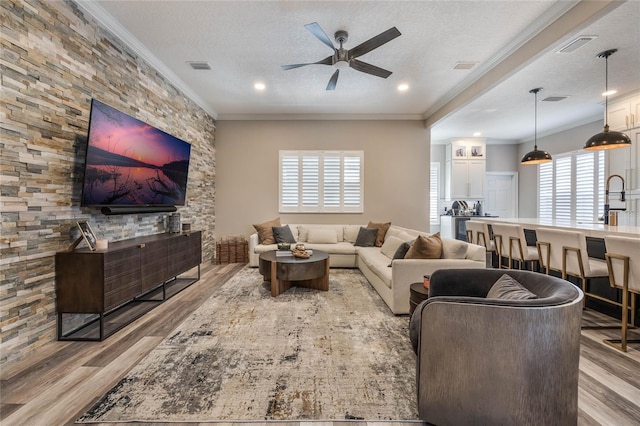 living room with ceiling fan, light hardwood / wood-style flooring, ornamental molding, and a textured ceiling