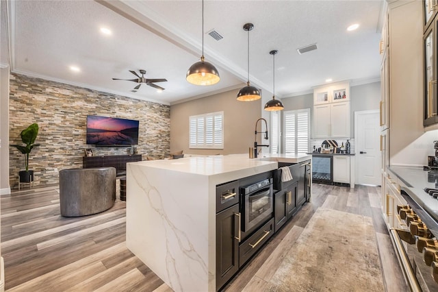 kitchen featuring ceiling fan, a kitchen island with sink, light wood-type flooring, hanging light fixtures, and sink