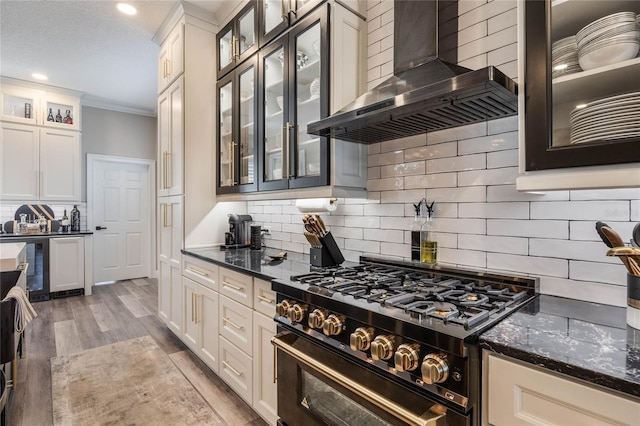 kitchen with backsplash, wall chimney range hood, dark stone countertops, hardwood / wood-style flooring, and high end stainless steel range oven