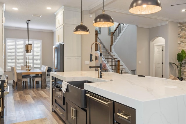 kitchen with high end fridge, decorative light fixtures, a kitchen island with sink, ornamental molding, and white cabinets