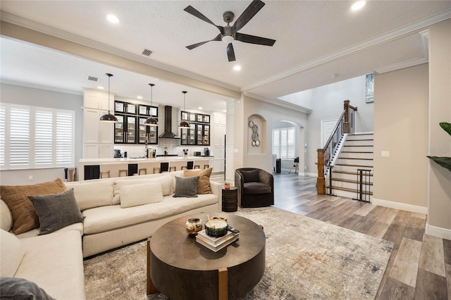 living room featuring ceiling fan, a textured ceiling, ornamental molding, and light hardwood / wood-style flooring