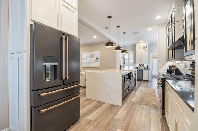 kitchen with pendant lighting, a center island with sink, white cabinetry, light wood-type flooring, and high quality appliances