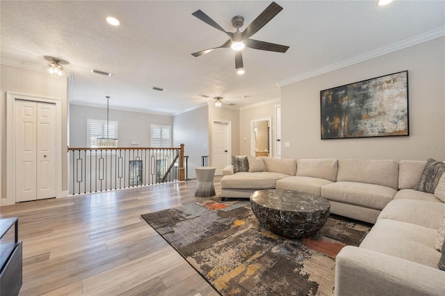 living room with a textured ceiling, ceiling fan, ornamental molding, and light hardwood / wood-style floors