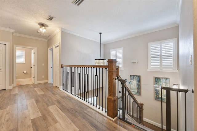 hallway with a textured ceiling, crown molding, and light hardwood / wood-style flooring