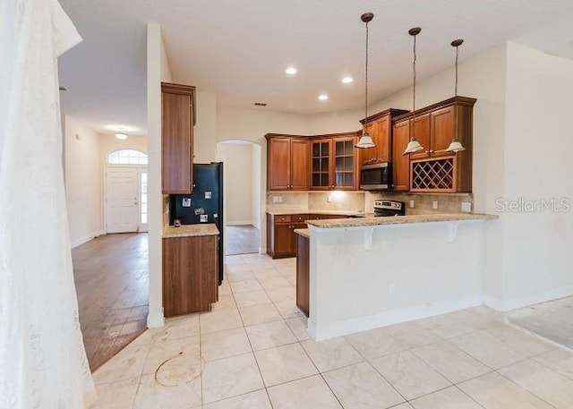 kitchen featuring kitchen peninsula, pendant lighting, a breakfast bar, decorative backsplash, and appliances with stainless steel finishes