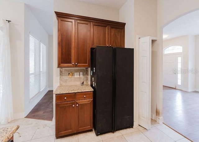 kitchen with black fridge, light stone countertops, light tile patterned floors, and backsplash