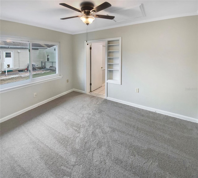 empty room featuring ceiling fan, crown molding, light colored carpet, and built in shelves