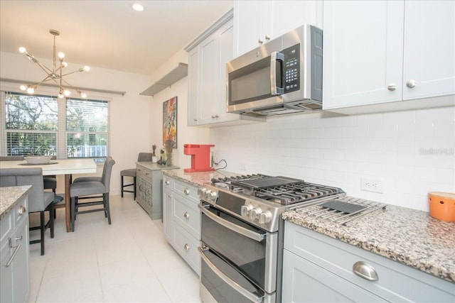 kitchen with pendant lighting, appliances with stainless steel finishes, light stone counters, decorative backsplash, and a chandelier