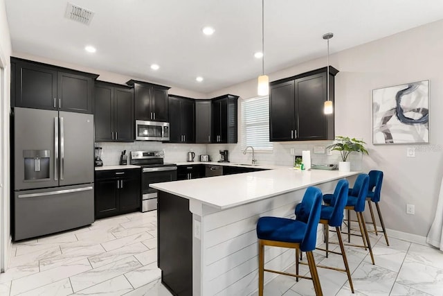 kitchen featuring pendant lighting, stainless steel appliances, a kitchen breakfast bar, backsplash, and kitchen peninsula