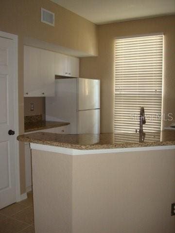 kitchen with white cabinetry, kitchen peninsula, tile patterned flooring, light stone countertops, and white refrigerator