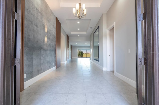 hall with light tile patterned flooring, an inviting chandelier, and a tray ceiling