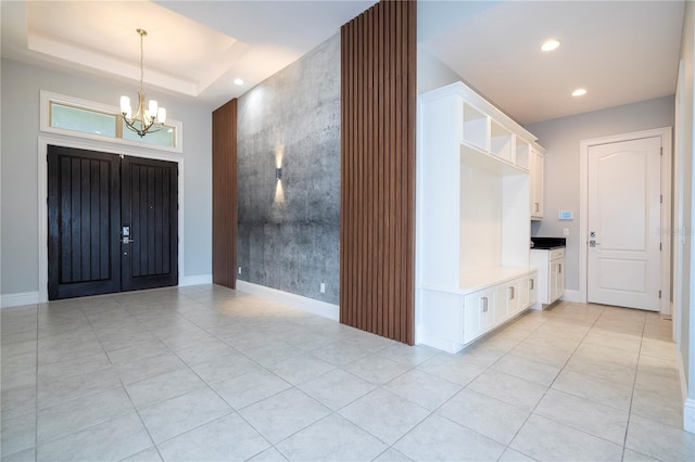 foyer entrance with light tile patterned floors, an inviting chandelier, and a tray ceiling