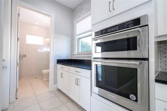 kitchen with white cabinets, stainless steel double oven, light tile patterned floors, and tile walls