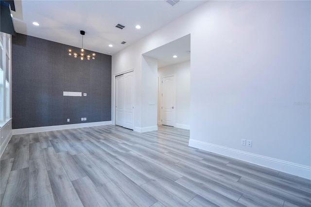 spare room featuring a notable chandelier and light wood-type flooring