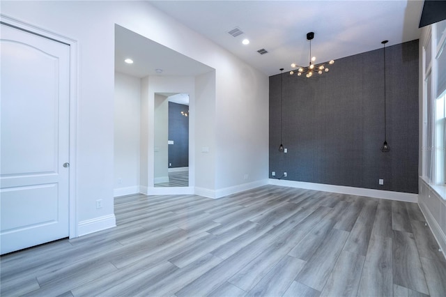 empty room with a notable chandelier and light hardwood / wood-style flooring