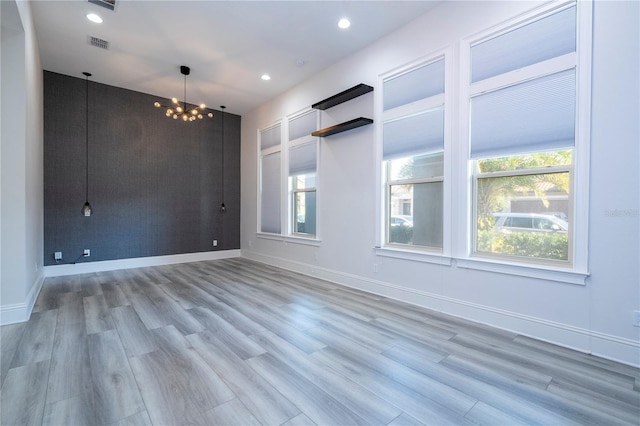 empty room featuring light wood-type flooring and a notable chandelier