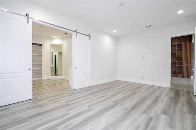 unfurnished room with a barn door and light hardwood / wood-style floors