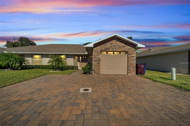 ranch-style home featuring decorative driveway, stucco siding, an attached garage, stone siding, and a front lawn