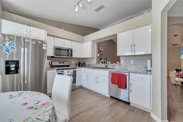 kitchen with lofted ceiling, sink, light wood-type flooring, stainless steel appliances, and white cabinets