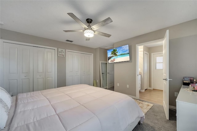 bedroom featuring multiple closets, light carpet, and ceiling fan