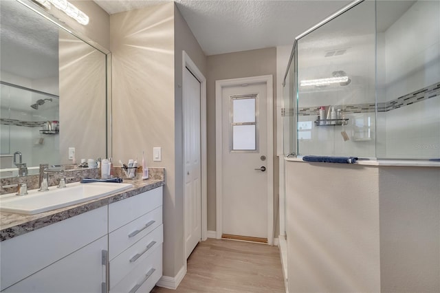 bathroom with vanity, hardwood / wood-style floors, a shower with shower door, and a textured ceiling