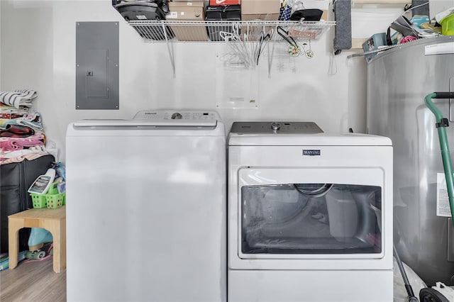 clothes washing area featuring electric panel, water heater, washing machine and clothes dryer, and light wood-type flooring