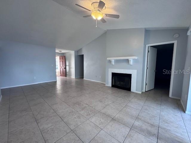 unfurnished living room featuring vaulted ceiling, ceiling fan, light tile patterned floors, and a textured ceiling