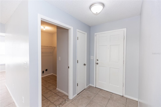 corridor with light tile patterned floors, baseboards, and a textured ceiling