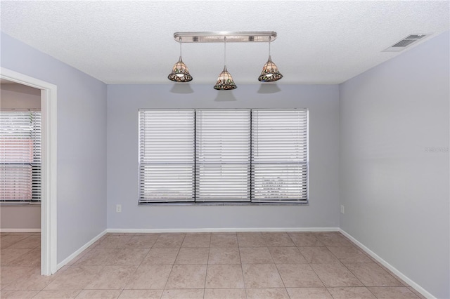 unfurnished dining area with baseboards, visible vents, a textured ceiling, and light tile patterned flooring